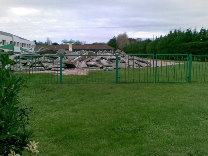 A pile of rubble near the outdoor pool with the old reception building to the left